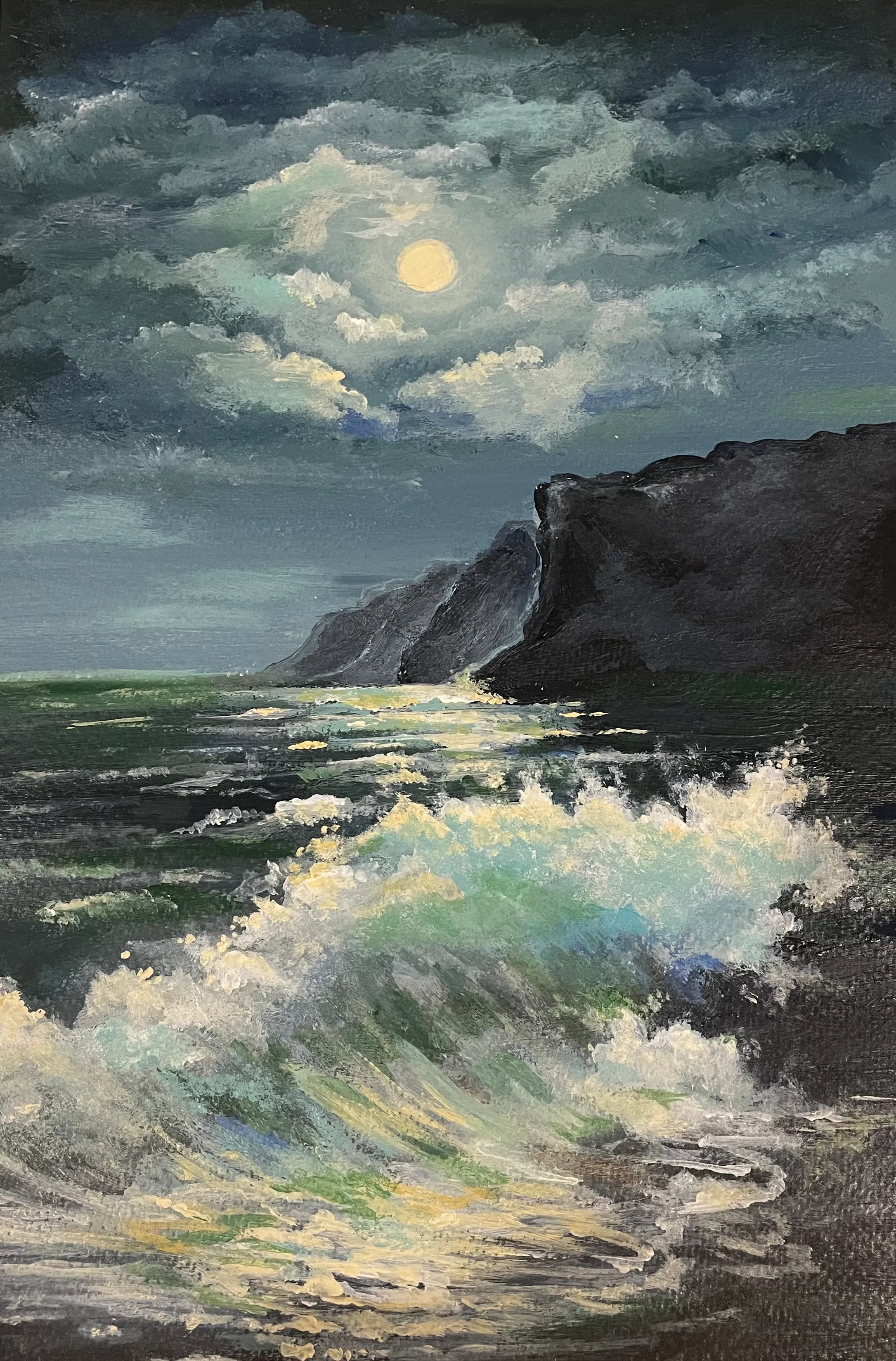 A full moon behind clouds illuminates turquoise waves breaking beside a dark coastal cliff.